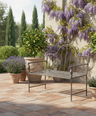 Metal bench on a patio with potted plants and a wisteria-covered wall.