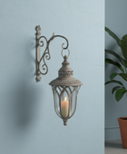 Decorative wall lantern with candle on a light blue wall next to a potted plant.
