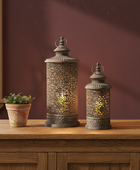 Decorative lanterns on a wooden surface with a potted plant against a maroon wall.