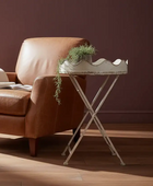 Brown leather armchair with a small metal table and plant against a dark red wall.