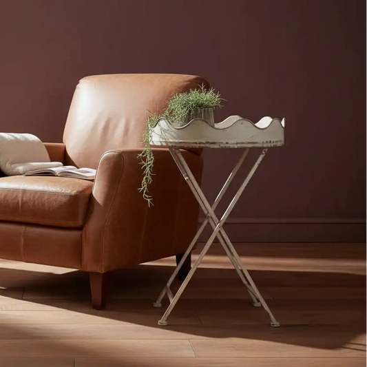 Brown leather armchair with a small metal table and plant against a dark red wall.