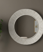 Round decorative mirror with a textured frame on a wall, next to a plant.