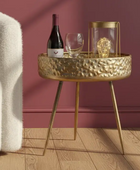 Gold side table with wine bottle, glasses, and decorative item against a red wall.