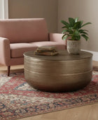 Round brown coffee table with a plant and books in a living room setting.