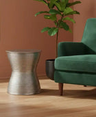 Green sofa with a textured metal side table and a potted plant in a room with a brown wall.