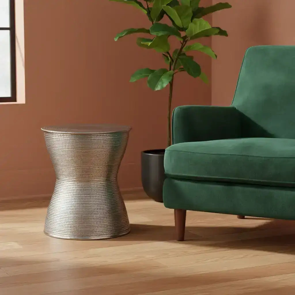 Green sofa with a textured metal side table and a potted plant in a room with a brown wall.