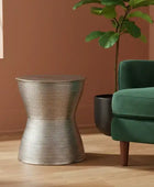 Silver side table next to a green armchair with a plant in the background