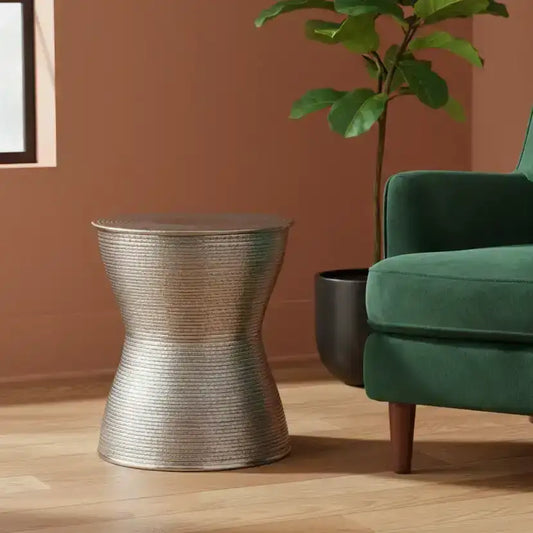 Silver side table next to a green armchair with a plant in the background
