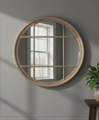 Round wooden-framed mirror on a gray wall with a plant on a table to the right.