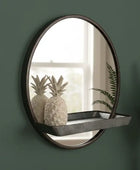 Round wall mirror with a shelf on a green wall, featuring decorative items.
