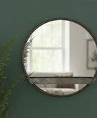 Round mirror with wooden frame on a green wall with a plant to the left.