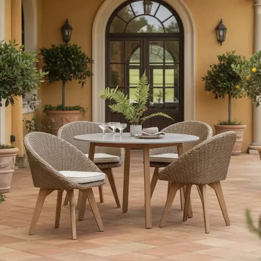 Outdoor patio set with round table and four chairs on a patio with plants and a building in the background.