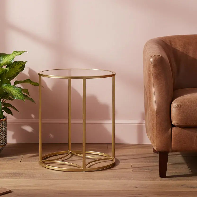 Gold side table in a living room with a pink wall and brown armchair.