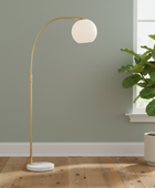 Modern floor lamp with a spherical shade next to a potted plant in a room with a green wall and wooden floor.