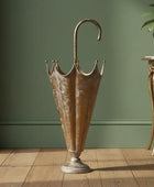 Bronze umbrella stand on a wooden floor with a green wall and plant in the background