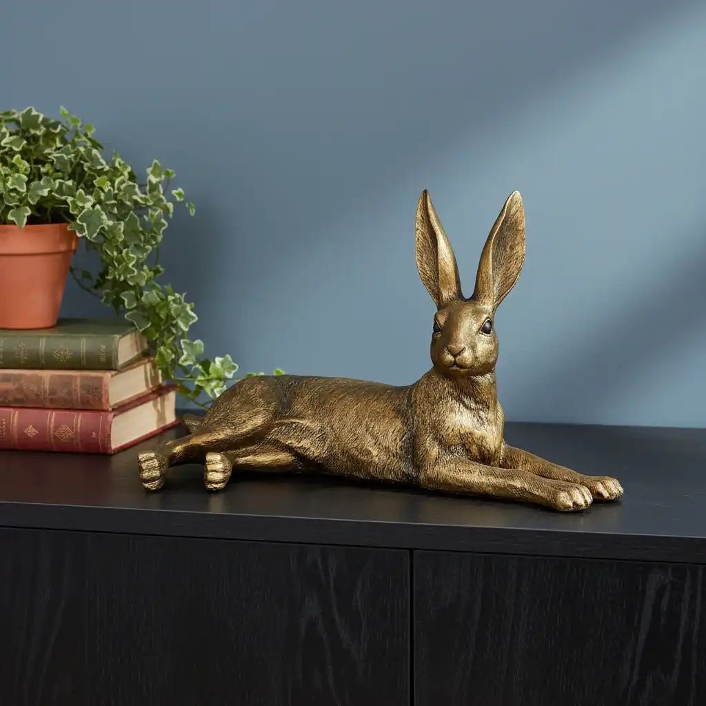 Bronze hare sculpture on a dark surface with books and a plant against a blue wall.