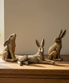 Three rabbit figurines on a wooden surface with a plant and book in the background.