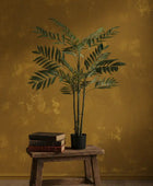 Potted plant on a wooden stool against a textured mustard yellow wall