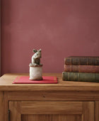 Wooden table with a decorative mouse figure and stack of books against a red wall.