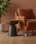 Brown armchair with a wooden side table and plant in a room with a brown wall.