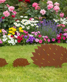 Three brown hedgehog-shaped garden decorations in front of a colorful flower bed.