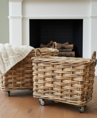 Two wicker baskets with wheels on a wooden floor in front of a fireplace.