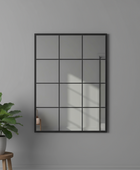 Wall mirror with grid design on a gray wall with a plant and stool in the foreground