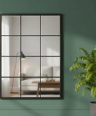 Decorative mirror with grid design on a green wall next to a potted plant