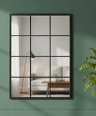 Decorative mirror with a grid design on a green wall, next to a potted plant.