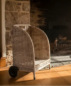 Wicker chair in front of a stone fireplace with a fire burning.