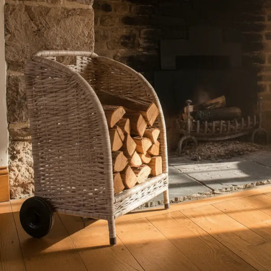Wicker log holder with stacked firewood in front of a stone fireplace.