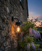 Wall-mounted light fixture on a stone wall with wisteria flowers in the foreground