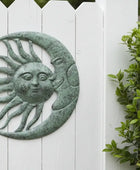 Decorative sun and moon wall art on a white picket fence with greenery.