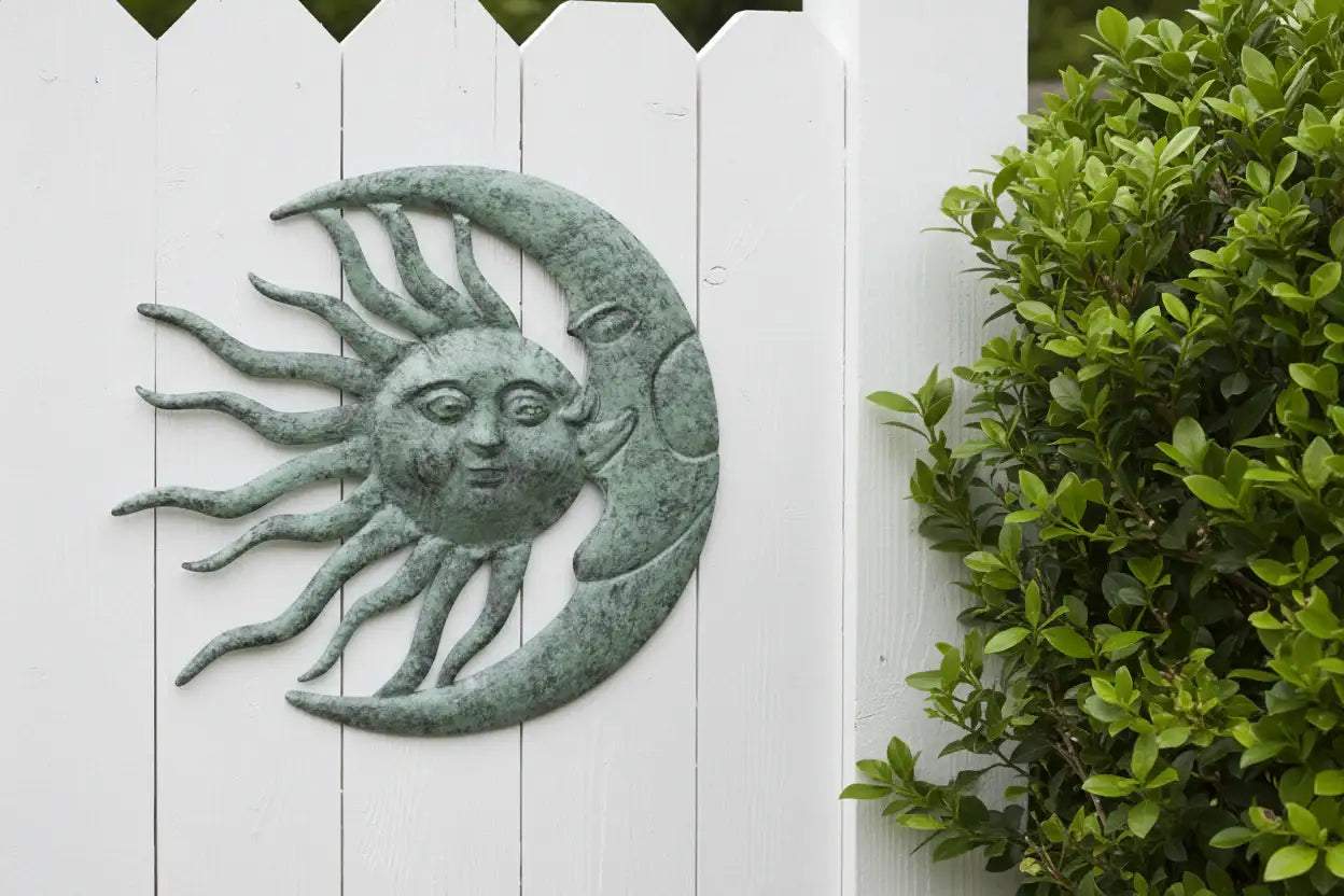 Decorative sun and moon wall art on a white picket fence with greenery.