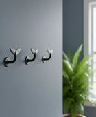 Three wall hooks on a gray wall with a plant in the corner