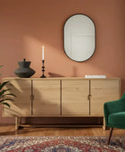 Wooden sideboard with decorative items against a pink wall, green armchair, and patterned rug.
