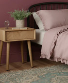 Wooden side table with a drawer, glass of water, and plant on a white background