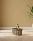 Wicker basket and potted plant on a wooden floor with a large window in a minimalistic room.
