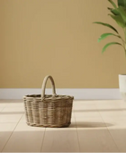Wicker basket on a wooden floor with a plant in the background