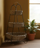 Three-tiered wicker basket stand against a yellow wall with a plant in the corner.