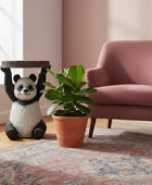Decorative panda figurine holding a plant next to a pink armchair in a room with a rug and window.