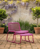 Pink outdoor chair and ottoman with a garden setting featuring plants and flowers.