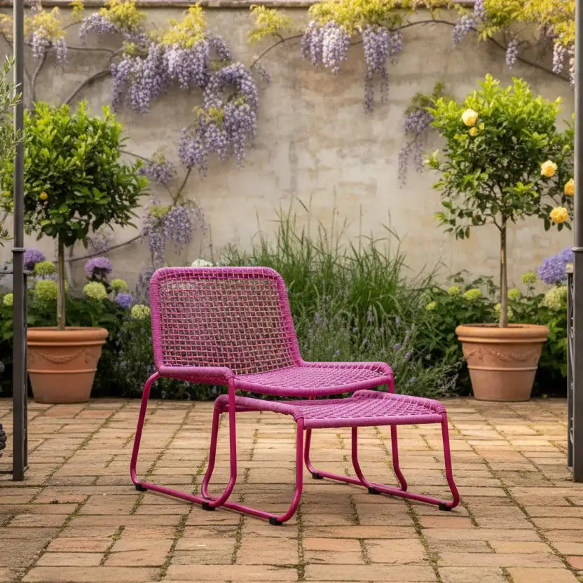 Pink outdoor chair and ottoman with a garden setting featuring plants and flowers.