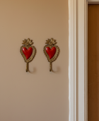 Two matching decorative wall hooks mounted on a beige wall, each featuring an ornate gold-tone heart-shaped frame with a glossy red heart center and a small floral detail above.