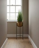 A tall green potted plant in a metallic gold pot on a black metal stand, placed in a minimalist hallway with beige walls and light wood floors.