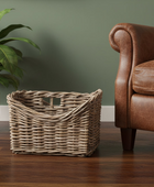 Wicker basket on a wooden floor next to a brown leather armchair against a green wall.