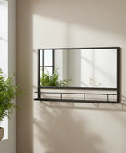 Wall-mounted mirror with shelf against a light wall, next to a window with plants.