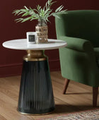 Round side table with marble top and black base next to a green armchair in a room.