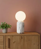 Table lamp with marble base and round glass shade on a wooden surface against a pink wall