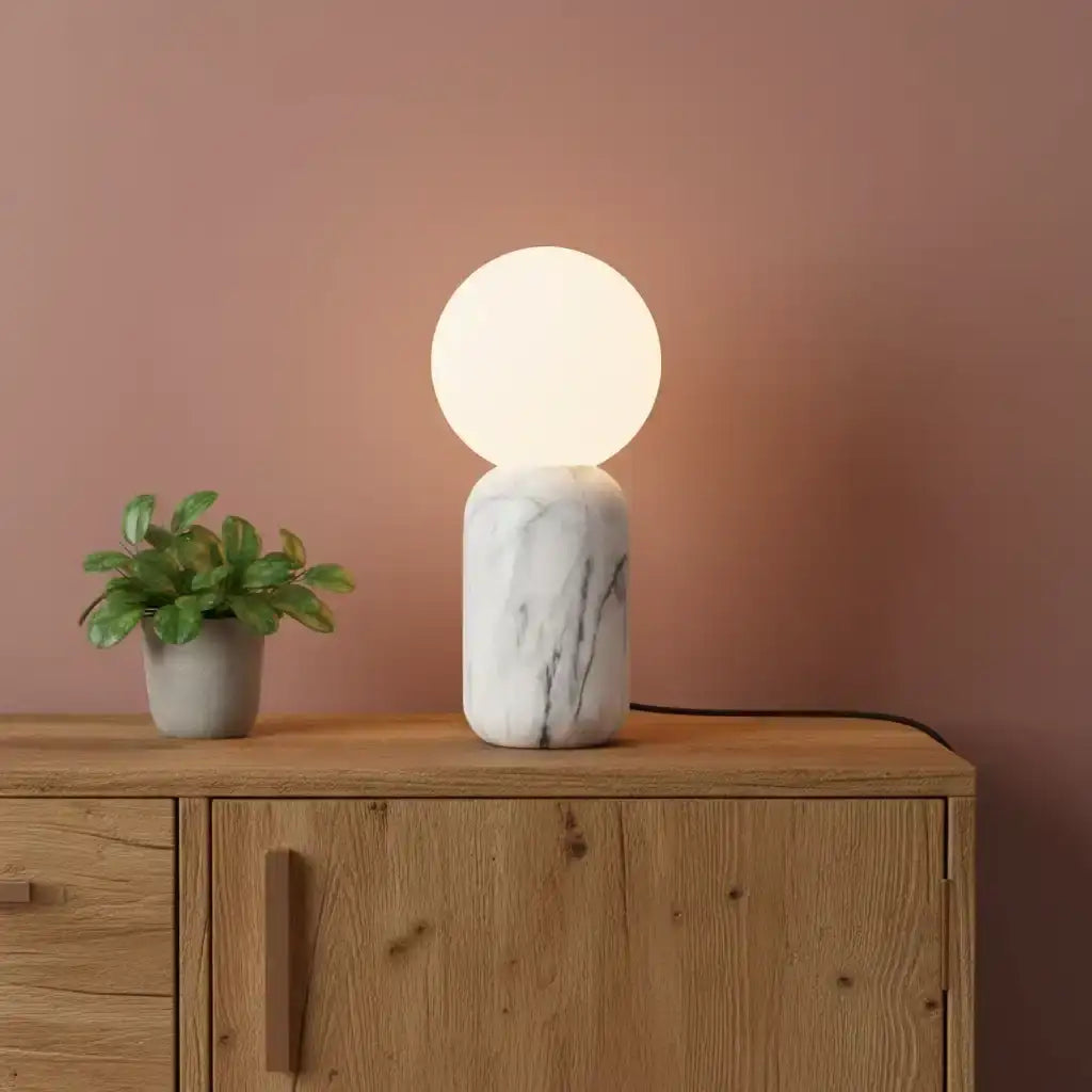 Table lamp with marble base and round glass shade on a wooden surface against a pink wall